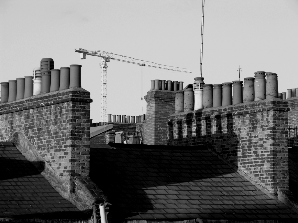 A row of chimney pots shown in black and white with a crane in the background.